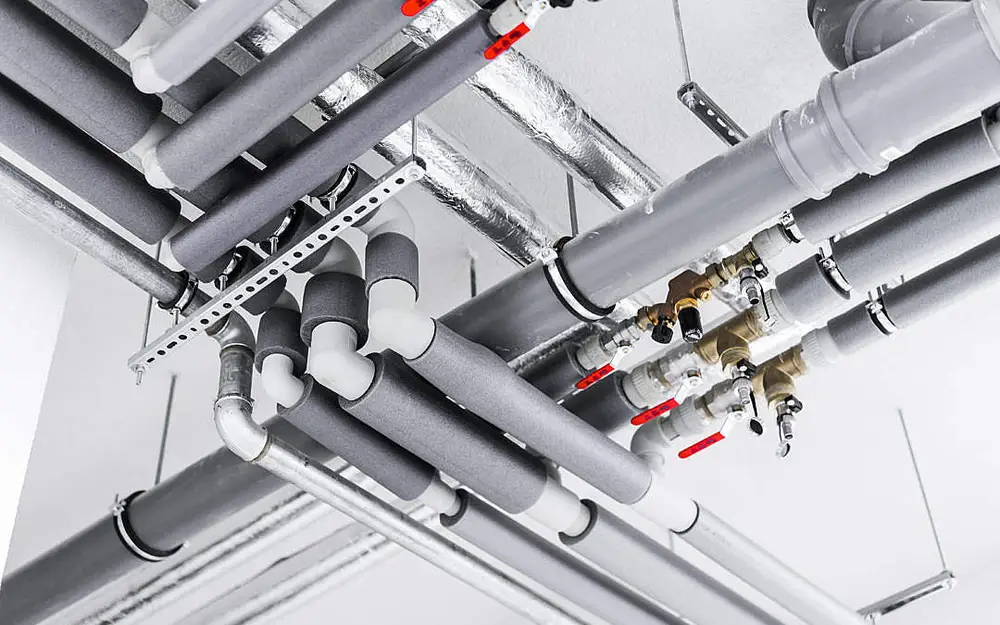 Insulated service pipe runs and valves fixed to the ceiling of a commercial plant space