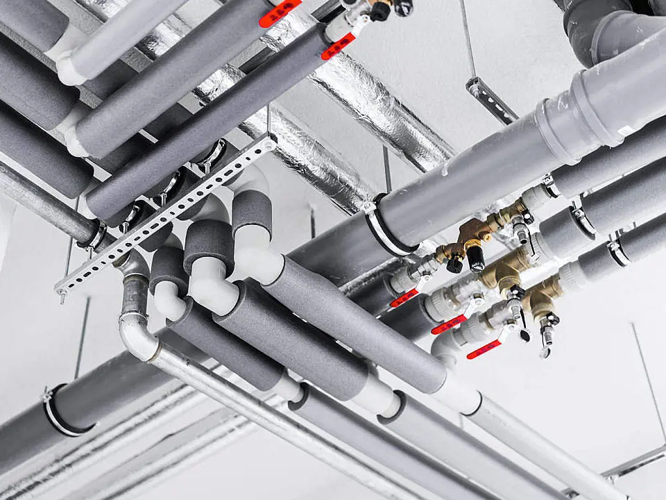 Insulated service pipe runs and valves fixed to the ceiling of a commercial plant space